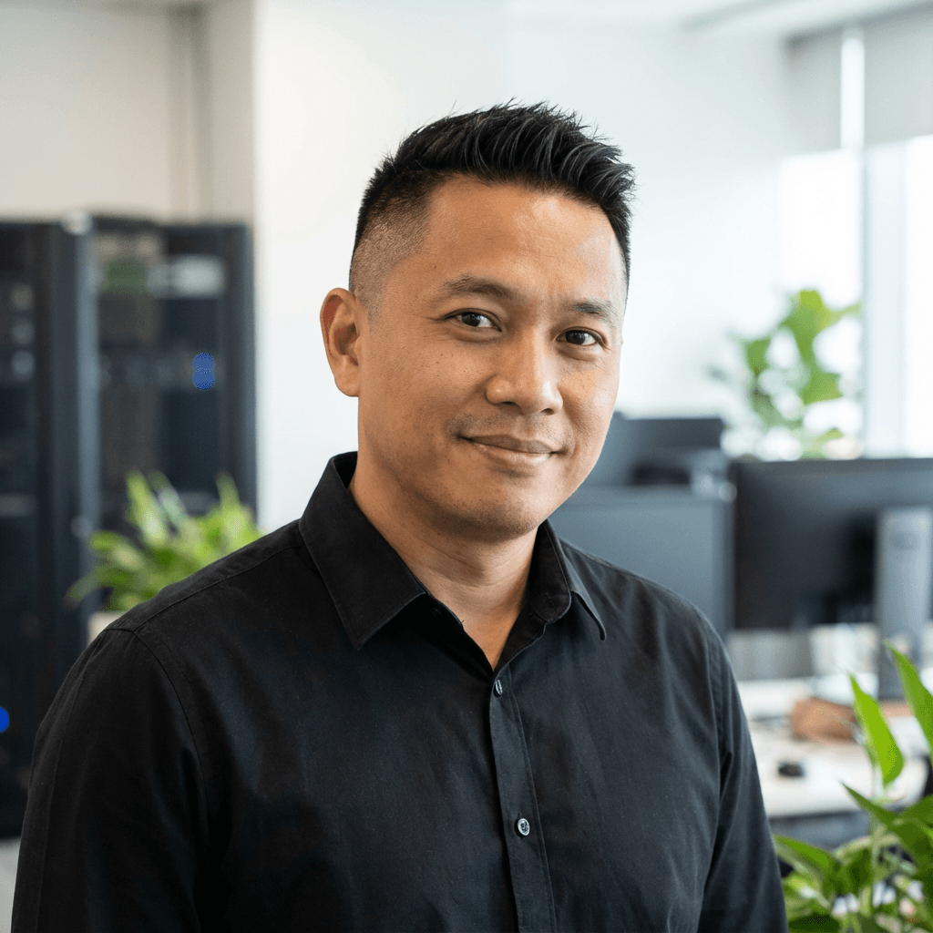 Smiling Asian man wearing a black button-down shirt in a bright, modern office setting.