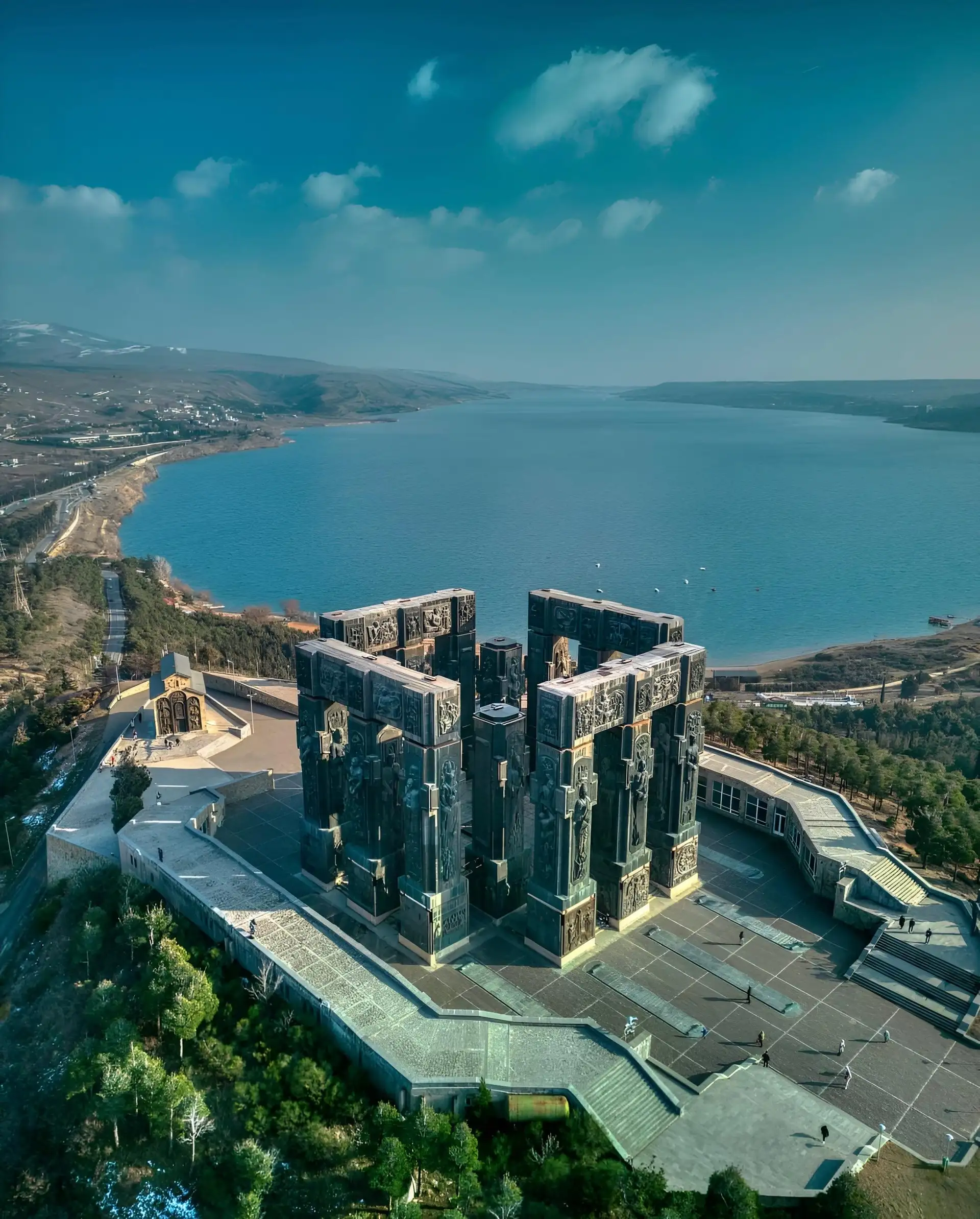 Massive bronze pillars of the Chronicle of Georgia monument overlooking a vast blue reservoir.